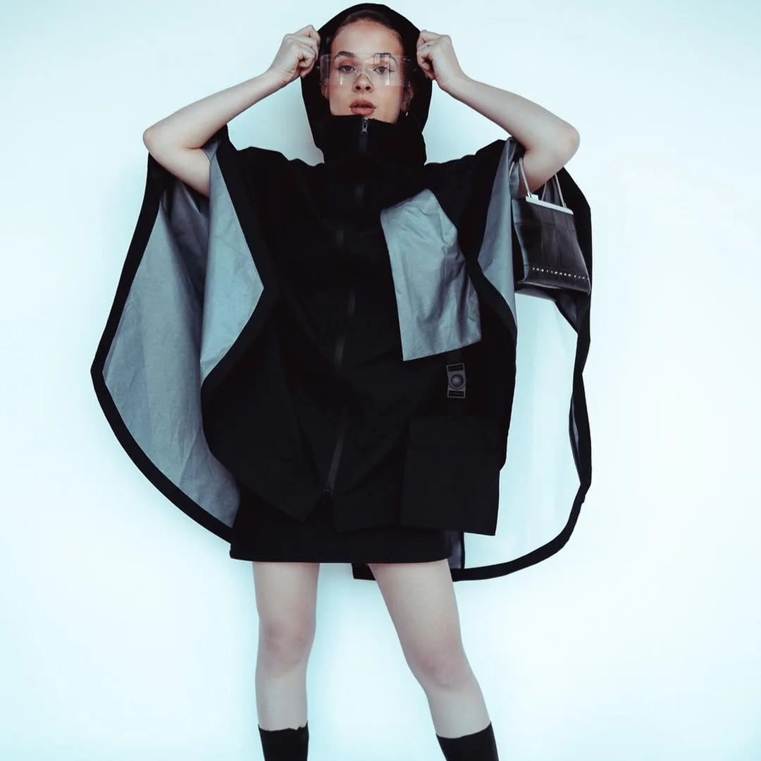 Female model in a futuristic black techwear poncho with clear visor glasses in a studio setting, cyberpunk-inspired Imaphotic fashion.